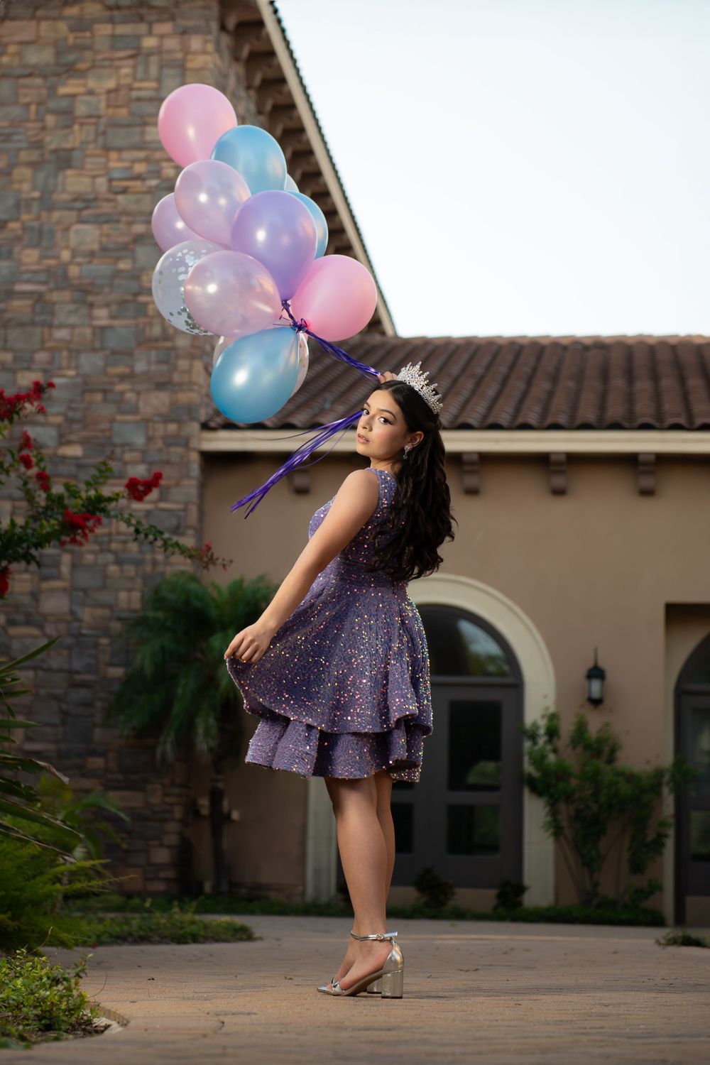 A twirling purple dress catches the light while colorful balloons float against a stone building backdrop.