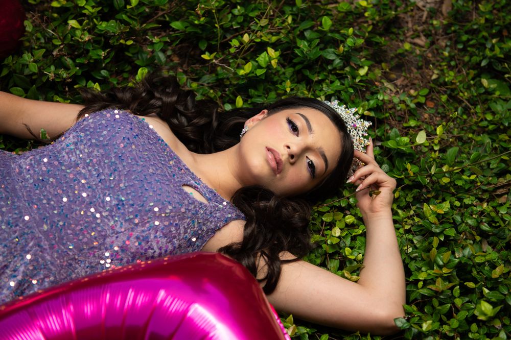 Elegant portrait with crown and sparkly dress against lush greenery.