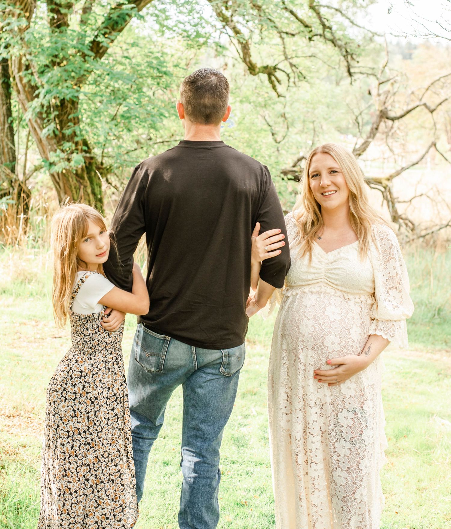 A family walks together through a sunlit garden path with trees and greenery surrounding them.