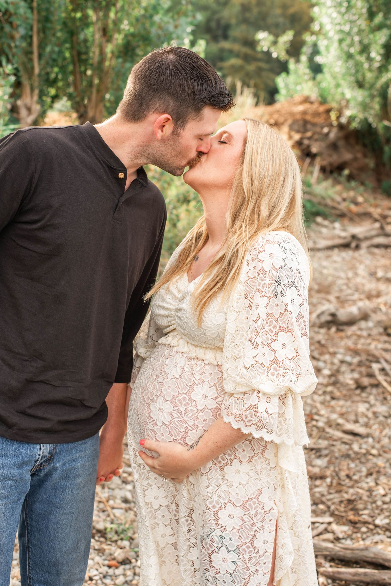 A couple shares intimate moments in an outdoor wooded setting wearing black and white lace outfits.