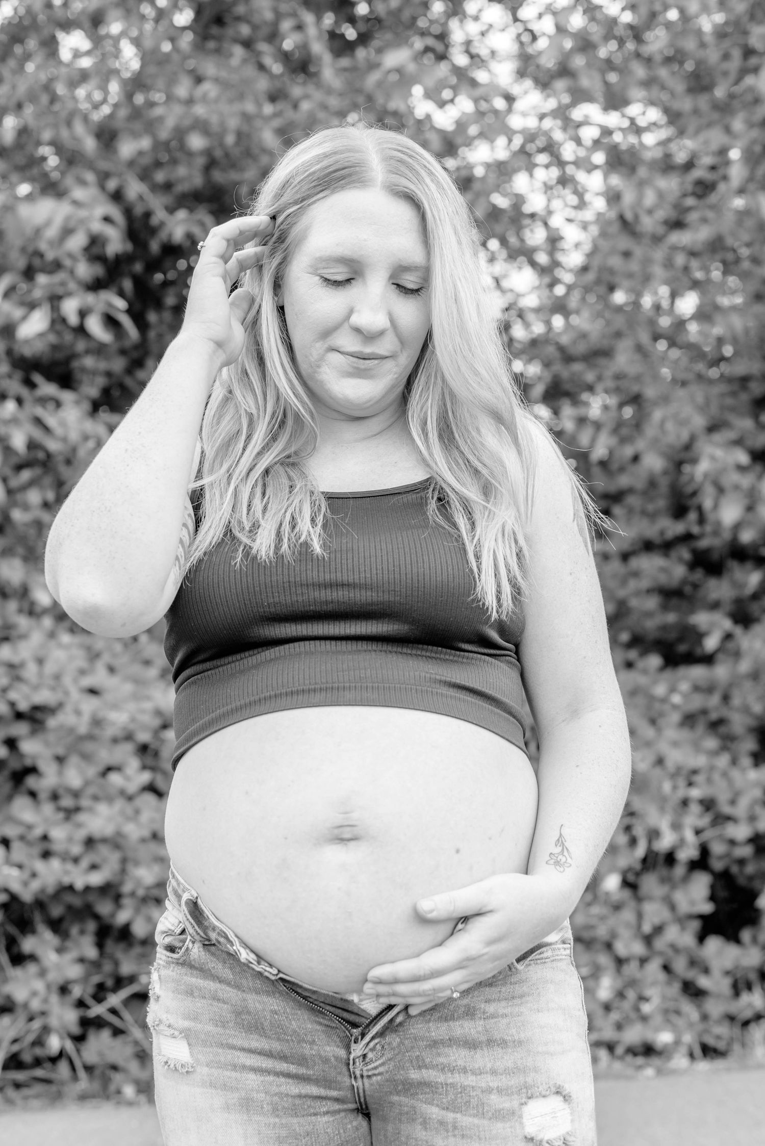 Black and white maternity photo series showing a pregnant woman's belly in casual attire against a natural outdoor backdrop.