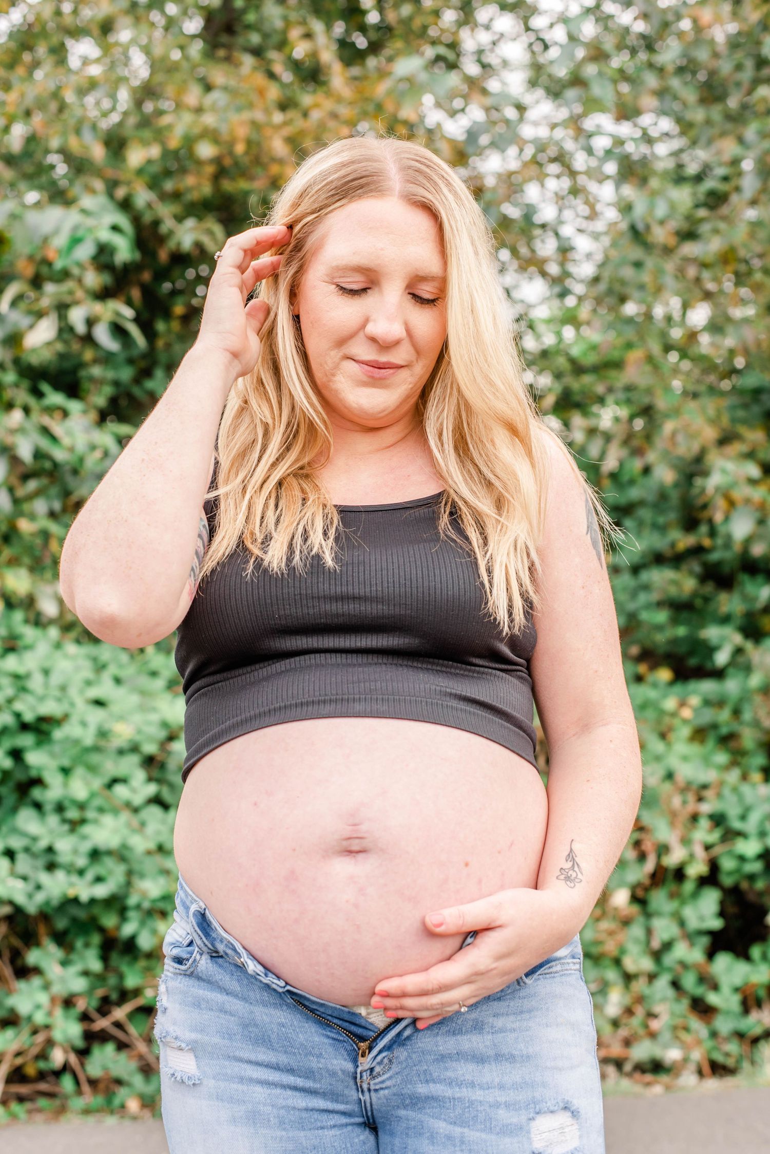 A series of maternity photos showing a pregnant person in a black tank top and jeans against a leafy green background.