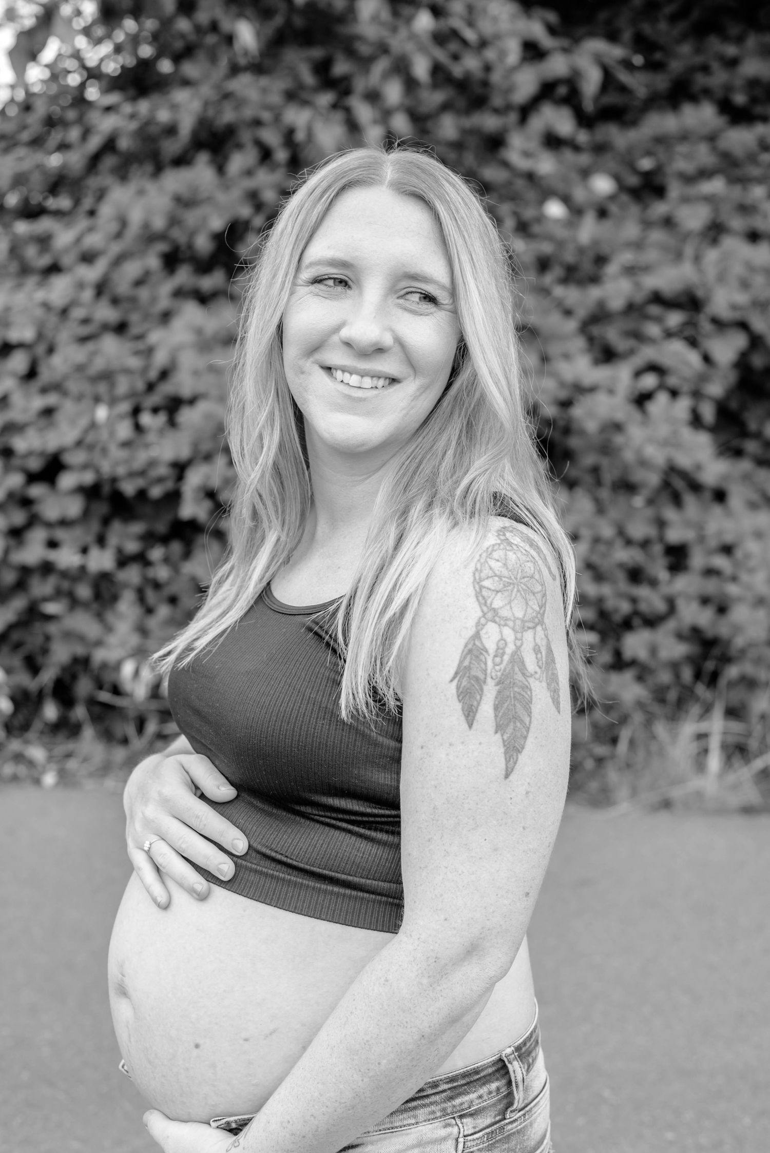 Black and white portrait series showing dreamcatcher tattoo on arm against natural outdoor background.