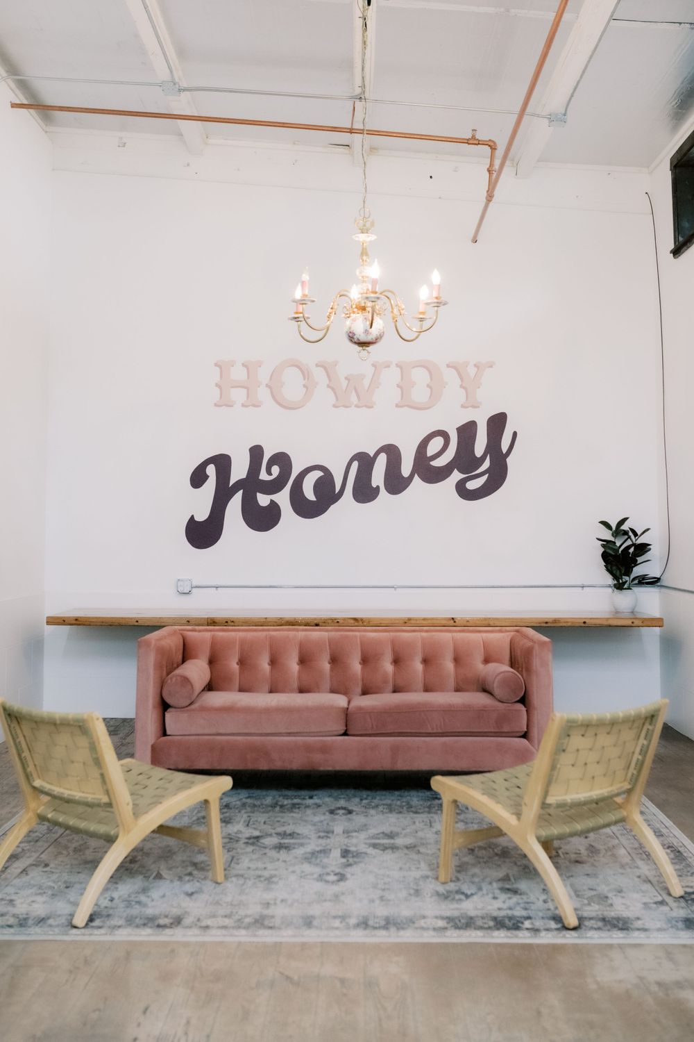 Modern lounge area with pink velvet sofa and 'Howdy Honey' wall text.