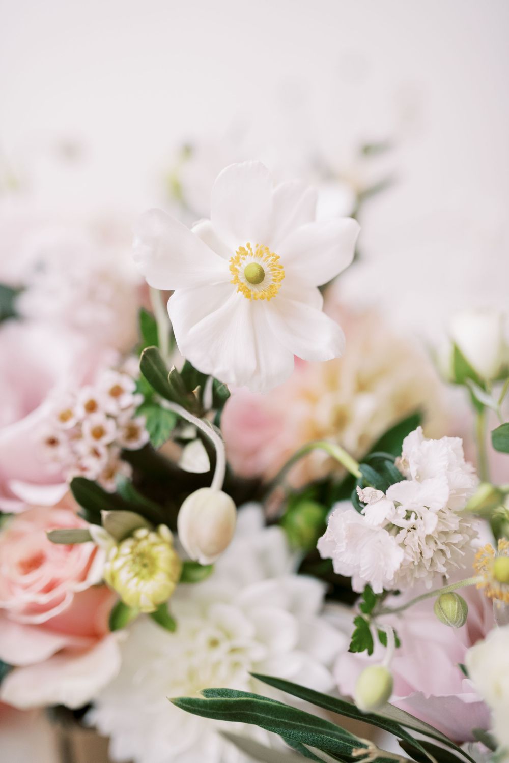 Delicate white and pink wedding bouquet with anemones and roses in soft focus.