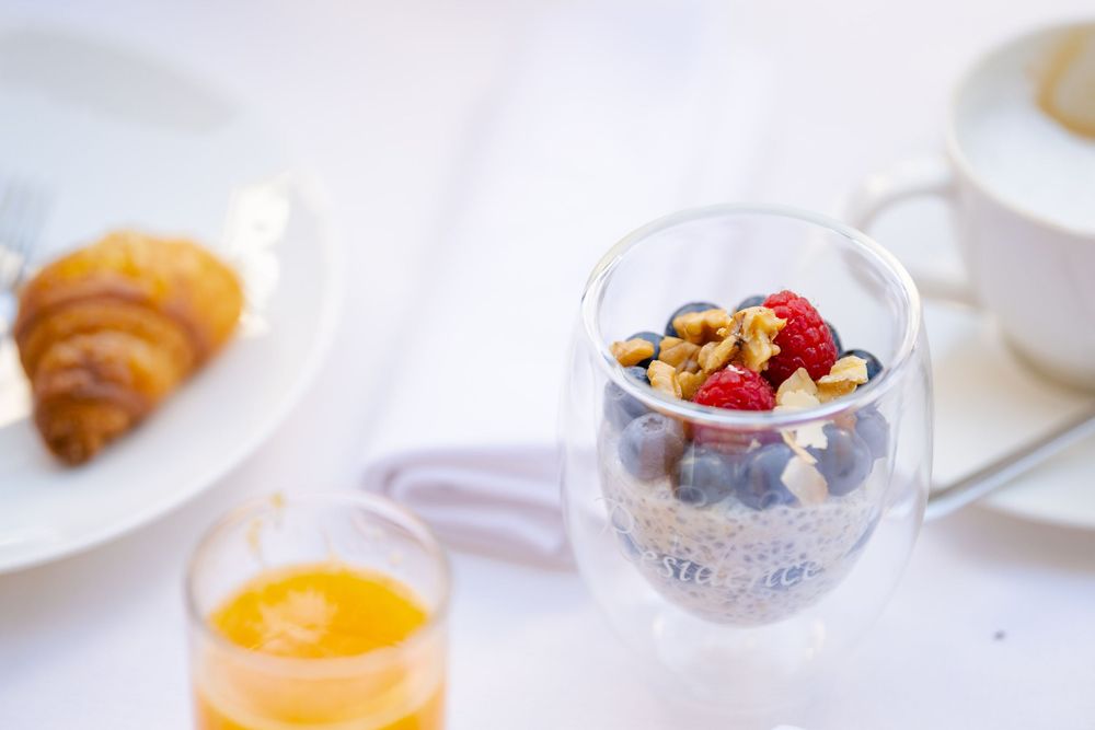 A healthy breakfast setup with a croissant, yogurt parfait with berries, and orange juice on a white tablecloth.