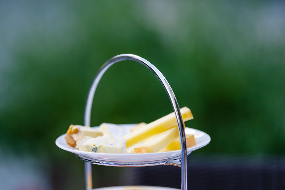 A tiered serving stand displays fresh fruit and cheese slices against a blurred green background.