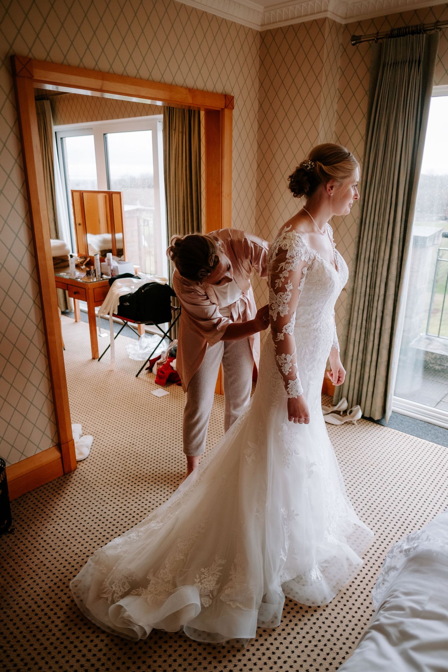 Wedding dress preparation in an elegant hotel room with patterned wallpaper.
