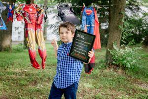 A blue checkered shirt is worn while posing with superhero costumes hanging in trees.