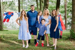 Family wearing coordinated blue outfits poses together outdoors with superhero costumes in background.
