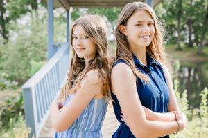 Two people in blue and light blue dresses stand back to back on a bridge.