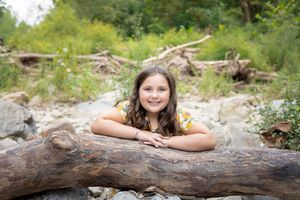 Outdoor portrait session captures resting poses on fallen log in natural wooded setting among scattered leaves and foliage.