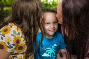A young child wearing a blue t-shirt with a palm tree design is shown between two others in a candid outdoor moment.