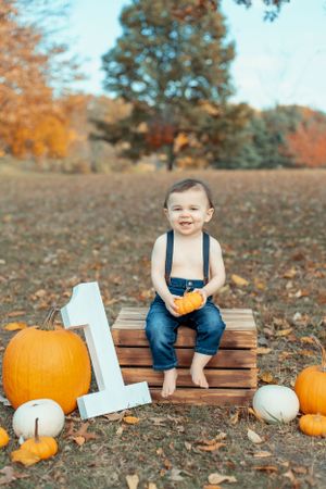 Fall pumpkin photo setup with wooden crates and white number one.