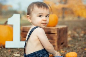 Side view portrait against orange autumn foliage with pumpkins and wooden number.
