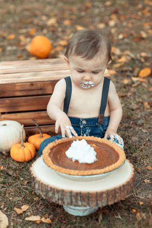 Small hands reaching for pumpkin pie with whipped cream on rustic wooden slice.