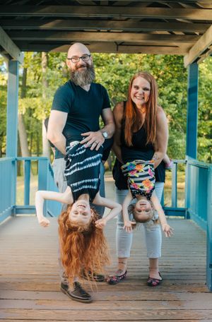 Fun family portrait with children hanging upside down on blue wooden gazebo.
