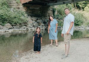 Family standing near a stream under rocky overhanging cliffs on a sunny day.