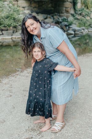 Mother and daughter sharing a close moment by a creek in summer attire.