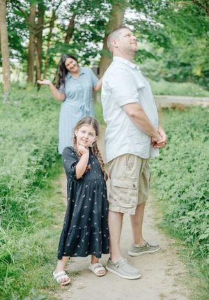 Family posing playfully on a green forest path during summer.