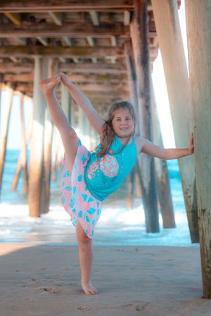 Girl performing dance move under pier wearing turquoise and coral outfit.