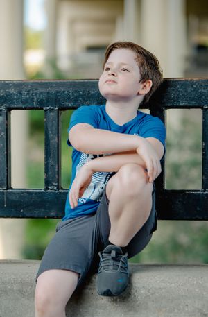 Boy sitting casually on black metal railing with crossed arms.