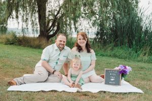 Family in coordinating outfits poses on picnic blanket with letter board.