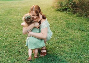 Two people in mint green outfits share a tender embrace on grassy lawn.