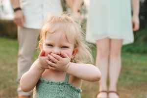 Young child in mint green dress giggles while covering mouth with hands.
