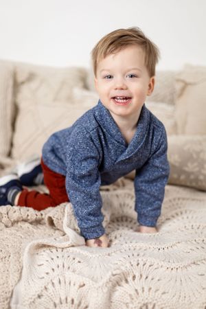 Smiling in blue sweater on cream knit blanket.