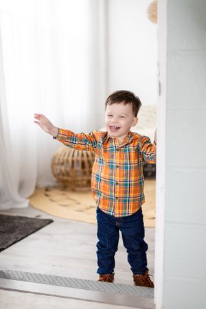 Joyful expression in orange plaid shirt by bright window.
