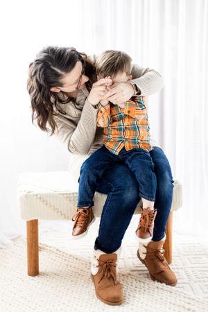 Two people sharing a playful moment while sitting on a wooden bench on a white carpet.