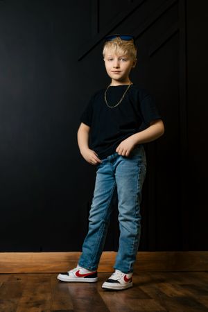 A youth in a black t-shirt and jeans poses against a dark background wearing a blue cap.
