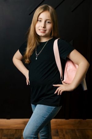 A youth posing in casual wear with a pink handbag against a dark background.