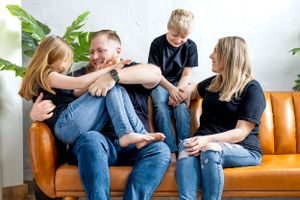 A playful family moment captured on a brown leather couch with everyone wearing casual attire.