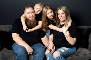 A family of four wearing matching black outfits poses together on a dark couch.