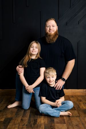 A studio portrait of a family wearing black shirts and jeans sitting together against a dark wall.