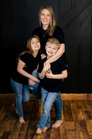 Family members in matching black shirts playfully pose together against a dark background.