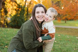 Parent and child enjoy an autumn photoshoot outdoors among vibrant fall foliage in matching green outfits.