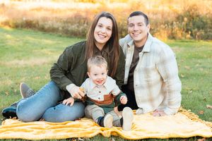 A family sits together on a yellow blanket in a grassy field during golden hour sunset.