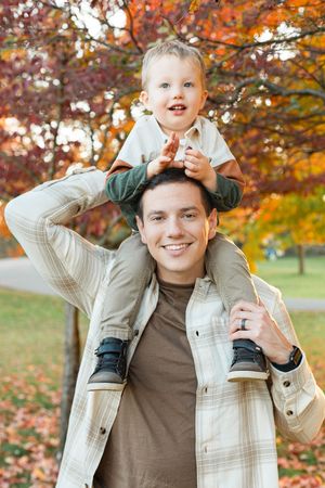 Parent and child playing together outdoors among colorful autumn trees and fallen leaves on a bright fall day.