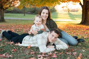 Family group lying together on autumn leaves during golden hour sunset photo session in park.