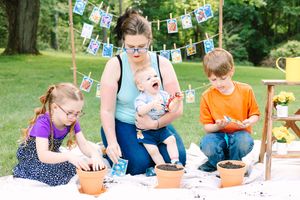 Family enjoying a planting activity outdoors with terracotta pots while decorative photos hang on string above them.