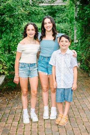 Several pairs of legs wearing summer outfits and shoes standing together on a brick pathway surrounded by greenery.