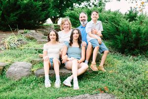 A group in casual summer attire relaxes outdoors on large rocks surrounded by lush greenery.