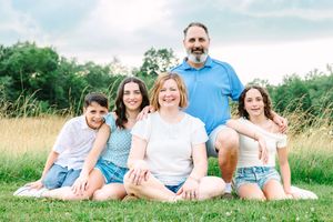 A happy family sits together on a white blanket in a sunny meadow with tall grass on a summer day.