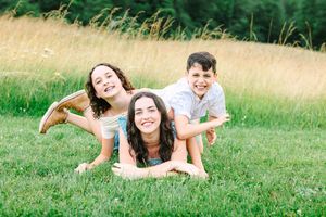 A playful sequence of people rolling and laughing together on a grassy meadow during a sunny summer day.