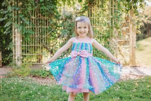 Sparkly blue and purple dress twirls in garden setting with trellis background.