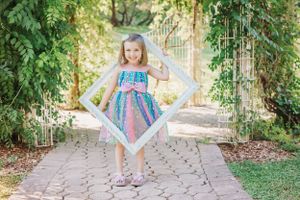 Colorful summer dress twirls in a garden path setting with lush greenery and brick pavers.