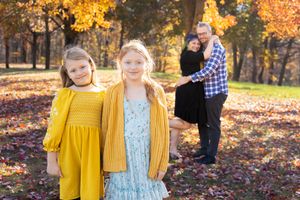 Family enjoying a fall photo session in a park with vibrant autumn foliage and yellow accents.